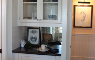 A white cabinet with glass doors and black counter top.