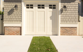 A white garage with two doors and grass in the driveway.