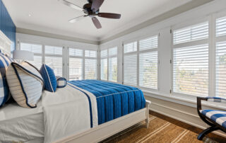 A bedroom with blue and white bedding, ceiling fan and large windows.