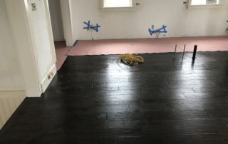 A room with black wood floors and blue tape on the floor.